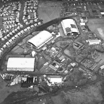 Oblique aerial view from ESE, centred on three hangars and various other buildings. The runway is visible in the top right-hand corner of the photograph.