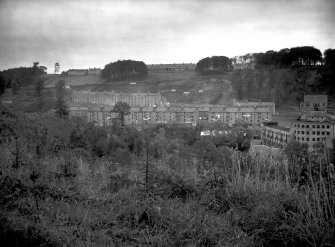 General view of New Lanark from the South bank of the Clyde showing Long Row, Braxfield Row and Mantilla Row, as well as un-roofed and propped shell of Mill No 1 to far right of view.