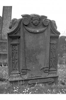 Stenton churchyard.
Patrick Logan d.1742. west face; winged cherub at top, blank inscription panel bordered by crossed spades and crossbones supended on ribbons. 'MOMENTO MORI' scroll and skull at base of stone.. Winged cherubs on slopes of tympanum.