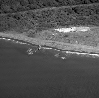 Oblique aerial view centred on the remains of the pile construction yard, scuttled ships, railway yard and railway, taken from the WSW.