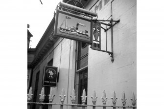Scanned image of John Hume photograph showing 43 Commercial Street, part of North Leith Citadel Railway Station..
View of signboard for the Steamboat Tavern and railing finials below.
