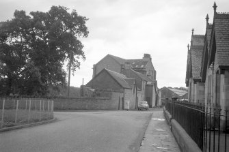 View looking SE showing workshops with main block of mill in background and with part of school in foreground