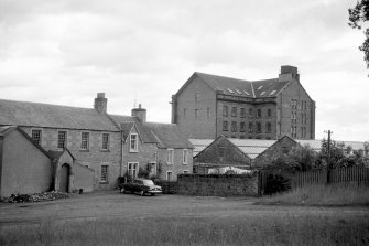 View from W showing SW front of houses with part of workshops in foreground and part of waterwheel house and main block of mill in background