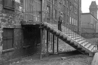 View from NW showing man standing on stairs which lead to main entrance on WSW front