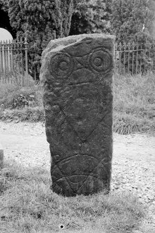 Pictish symbol stone standing in kirkyard. View of face, showing double-disc and Z-rod, and two crescent and V-rods.
Half-plate glass negative.