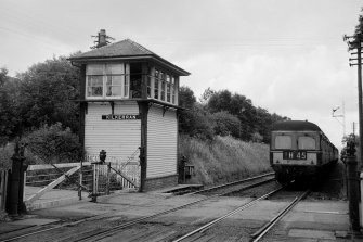 View from SSW showing SW and SE fronts of signal box with level crossing gates on left and train on right