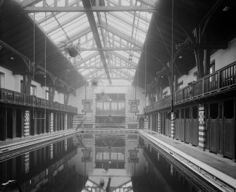Interior view of the pool area showing trapeze and rings over pool, and changing rooms at side of pool in the Public Baths and Gymnasium, Primrose Street, Alloa.
