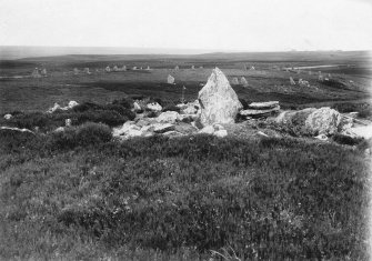 General view of horse-shoe shaped stone setting, with cairn in the foreground.