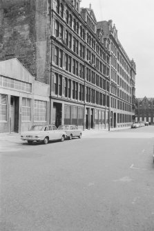 View from N showing WNW front of warehouse with part of number 24 in foreground and factory in background