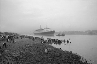 View looking SE showing QE II on River Clyde approaching Bowling with remains of pier in foreground