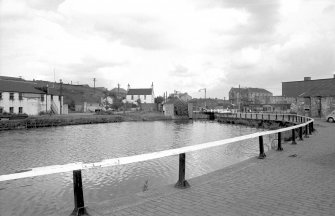 General view looking ENE showing old basin with part of workshops on left, canal house in centre and remains of houses on right