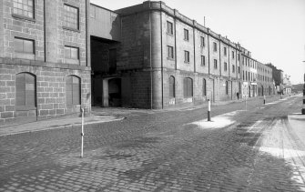 View from W showing SSW front and part of WNW front of E building with part of main building of flour mill in foreground and numbers 77-81 Waterloo Quay in background