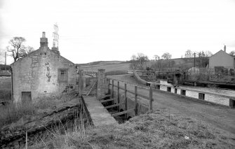 View from WNW showing N front of overflow with W front of cottages on left and bridge in background