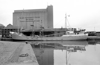 View from SW showing boat in harbour with part of grain wharf warehouses behind and grain silo in background