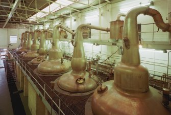 Elevated ground view from WNW within Still House, showing row of 8 stills, all but 2 of which were built by A.Forsyth of Rothes. The stills, which are coal fired, are arranged with wash and spirit stills in pairs, the latter being the smaller stills (with the more rounded necks).
Digital image of C 23610 CN.