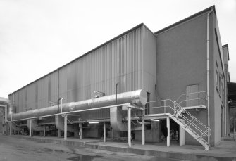 General exterior view from SE of Still House, showing rosw of chain-grate "Triumph" stokers feeding coal to the 8 stills within, and the flues and ash disposal pipes emerging from the side of the building.
Digital image of C 23611.