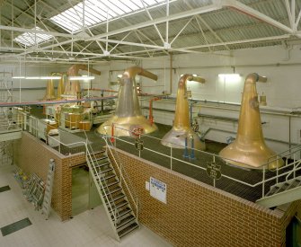 Benrinnes Distillery
Still House (item 7 on plan): elevated interior view from north, showing six copper pot stills, all of which are heated by steam coils.  The two larger stills in the centre are Wash Stills.  This distillery has a triple distillation process, which explains the presence of two low wines stills on either side of the Wash Stills.
Digital image of D 39117 CN.