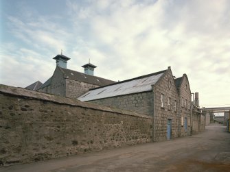 View from NW of main production block of distillery, showing ornate gables of the Tun Room and Mash House, with Malt Bins and Kilns in background, and Still House (R).
Digital image of C 64415 CN.