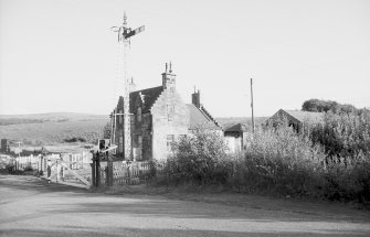View from NNW showing part of NW and NE fronts of down platform building with signal and level crossing gates in foreground