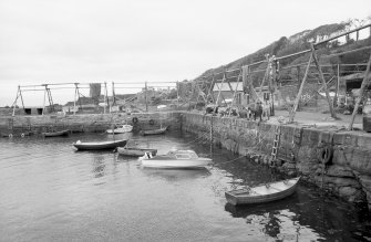 View from SW showing boats in harbour with wooden frames for net drying in background