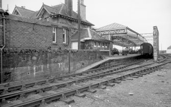View from NNE showing station building, glazed umbrella roof and supporting rubble wall