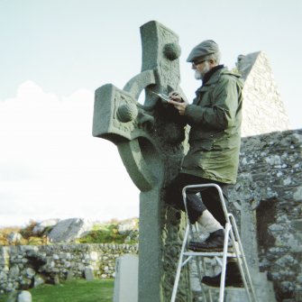 View of Ian G Scott, on ladder, making corrections to his drawing of the Kildalton Cross.