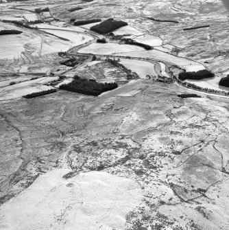 Raeburnfoot, oblique aerial view, taken from the NW, centred on a bank barrow, with ring-enclosures, enclosures and a Roman Fort to the top of the photograph.