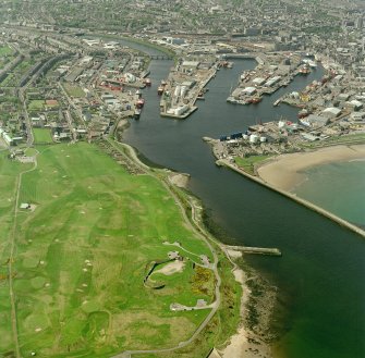 Oblique aerial view centred on the remains of the coastal battery with breakwater adjacent and harbour in background, taken from the E.