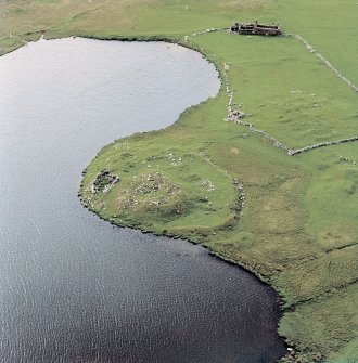 Oblique aerial view centred on the remains of the broch with the remains of the buildings, burnt mound and croft buildings adjacent, taken from the ESE.