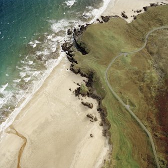 Oblique aerial view centred on the remains of the dun with the remains of the possible promontory fort, lazy beds and possible shieling-hut adjacent, taken from the NW.