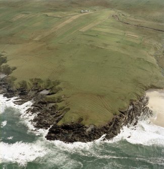 Oblique aerial view centred on the remains of the dun and building with the remains of lazy beds adjacent, taken from the WNW.