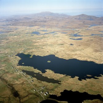 General oblique aerial view looking across the township and the remains of the dun towards Dalabrog, and Beinn Mhor in the distance, taken from the SW.