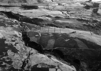 Oblique aerial view centred on the remains of a hut circle, field system, farmstead and rig at Redcastle and Blackhills, looking to the SW.