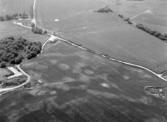 Oblique aerial view centred on the cropmarks of the timber hall, ring ditch, enclosures and pits at Mondobbo House, looking to the S.