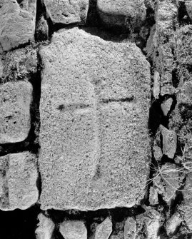 Photograph of cross-incised stone built into wall of farm building.