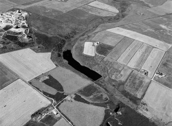 Oblique aerial view centred on the Den of Boddam reservoir, flint mines and lithic working site with RAF Buchan radar station adjacent, looking to the WSW.