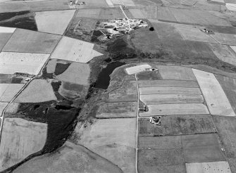 Oblique aerial view centred on the Den of Boddam reservoir, flint mines and lithic working site with RAF Buchan radar station adjacent, looking to the SSW.
