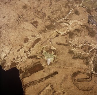 Oblique aerial view centred on the remains of the chambered cairn, taken from the W.