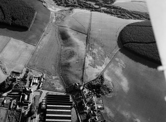 Oblique aerial view centred on the remains of the earthwork,  cropmarks of a rectilinear enclosure and pits at Thomshill with the Glenlossie distillery adjacent, looking to the WSW.