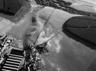 Oblique aerial view centred on the remains of the earthwork,  cropmarks of a rectilinear enclosure and pits at Thomshill with the Glenlossie distillery adjacent, looking to the SW.
