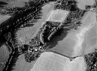 Oblique aerial view centred on the remains of the chambered cairns at Balnuaran of Clava with the farmstead adjacent, looking to the NE.
