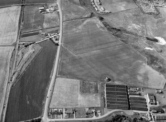 Oblique aerial view centred on the cropmarks of the ring ditch, pits and windmill at Sandend with Glenglassaugh Distillery adjacent, looking to the WNW.