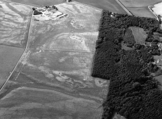 Oblique aerial view centred on the cropmarks of an unenclosed settlement, ring ditches, enclosures and pits at Craigston Castle with Fintry farmstead adjacent, looking to the W.