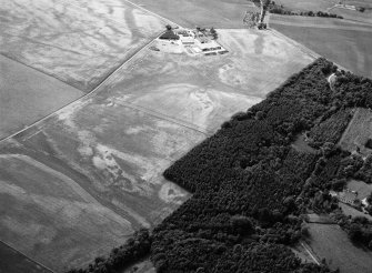 Oblique aerial view centred on the cropmarks of an unenclosed settlement, ring ditches, enclosures and pits at Craigston Castle with Fintry farmstead adjacent, looking to the WSW.