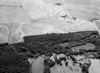 Oblique aerial view centred on Craigston Castle with the cropmarks of an unenclosed settlement, ring ditches, enclosures and pits adjacent, looking to the SW.