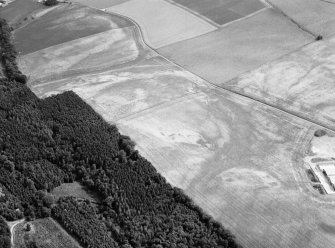 Oblique aerial view centred on the cropmarks of an unenclosed settlement, ring ditches, enclosures and pits at Craigston Castle, looking to the SE.