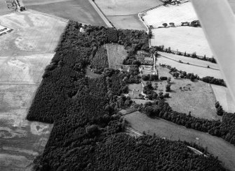Oblique aerial view centred on Craigston Castle with the cropmarks of an unenclosed settlement, ring ditches, enclosures and pits adjacent, looking to the WNW.