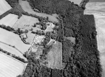 Oblique aerial view centred on Craigston Castle with the cropmarks of an unenclosed settlement, ring ditches, enclosures and pits adjacent, looking to the ESE.