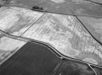 Oblique aerial view centred on the cropmarks of the unenclosed settlement and pits at West Mains of Hedderwick, looking to the SE.