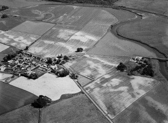 General oblique aerial view centred on the cropmarks of the barrow, enclosures, roundhouses, souterrain, pits and rig at Hatton of Fintray with the village adjacent, looking to the ESE.